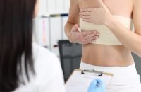 Woman with elastic bandage on her chest showing breast doctor to mammologist 4k movie. Mammoplasty surgical treatment of breast cancer concept