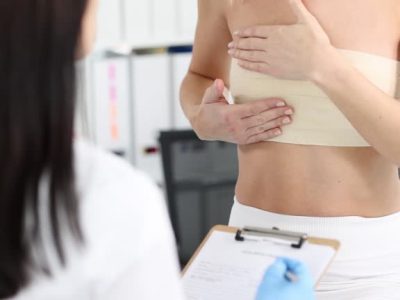 Woman with elastic bandage on her chest showing breast doctor to mammologist 4k movie. Mammoplasty surgical treatment of breast cancer concept